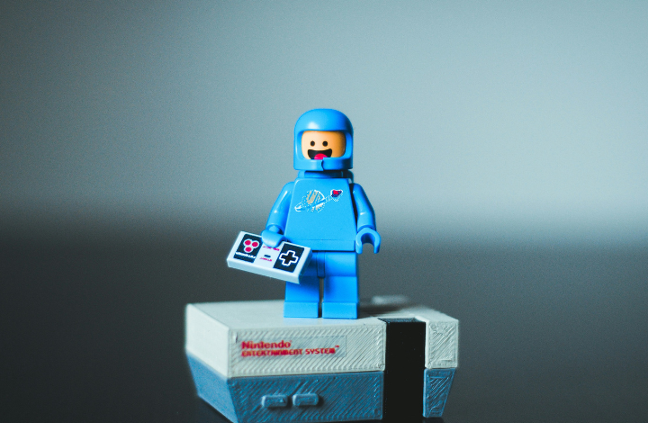 Blue Lego spaceman stands on a Lego NES console holding a controller.