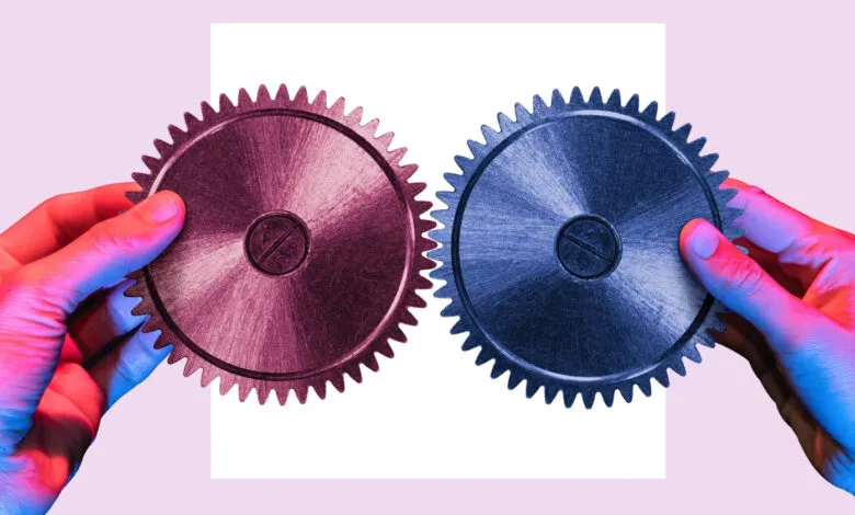 Two hands holding gears, one red and one blue, against a white backdrop.