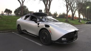 Silver autonomous vehicle with sensor array parked in lot.