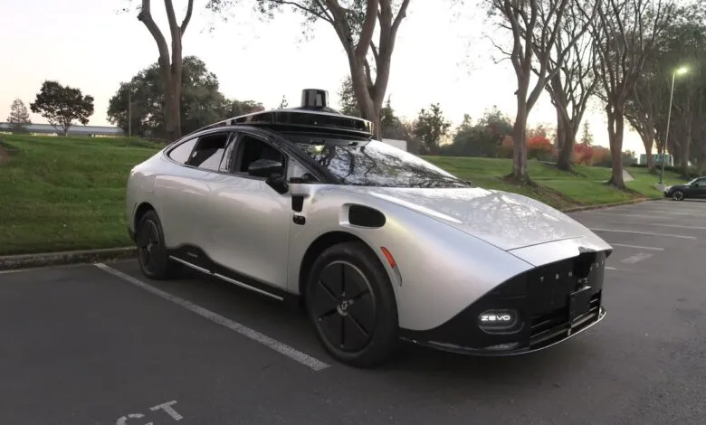 Silver autonomous vehicle with sensor array parked in lot.