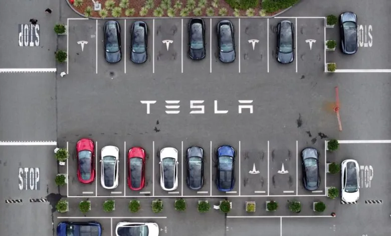 Aerial view of Tesla parking lot with cars and company logo.