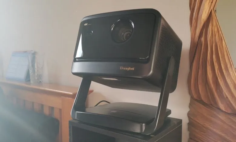 Black Dangbei 4K projector on stand, positioned on a black shelf.