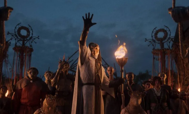 A masked figure raises hand amidst a diverse crowd in a fantasy setting.