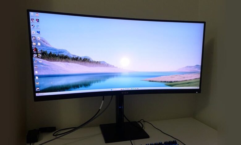 Curved monitor displays serene landscape with mountains, water, and a rising sun.