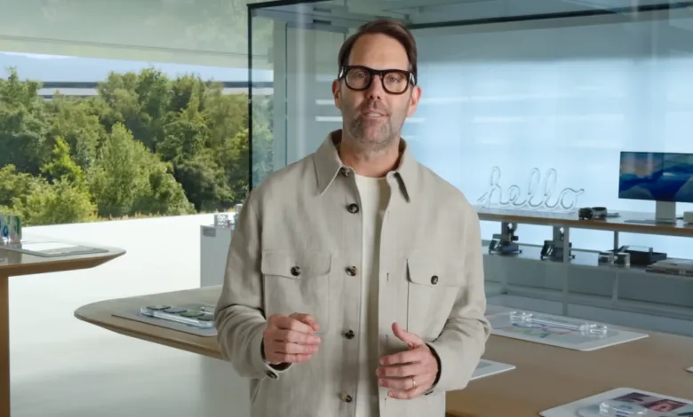 Man with glasses in light jacket stands in modern office space.
