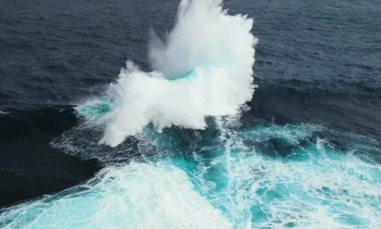 Powerful ocean wave crashing, creating a white water pillar.