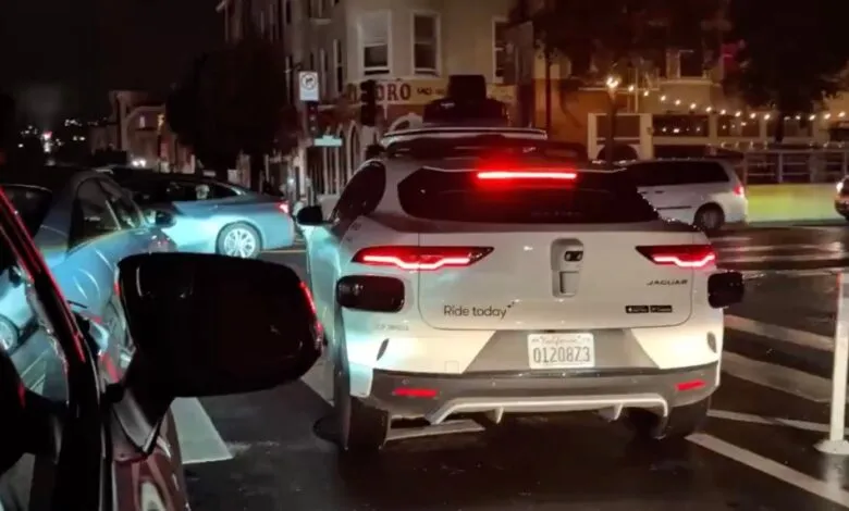 Waymo self-driving Jaguar I-Pace with sensors on a city street at night.