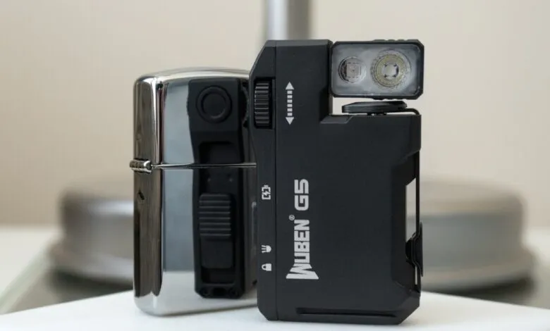 Wuben G5 flashlight next to a chrome lighter on a white surface.