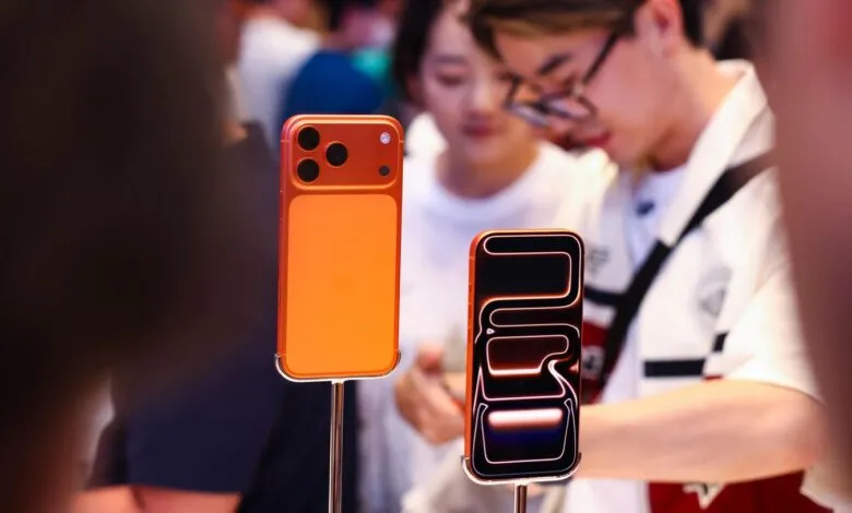 Two orange smartphones displayed on stands with people in the background.