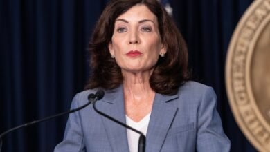 Kathy Hochul stands at a podium with a serious expression.