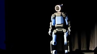 Blue and gray robot stands on stage with a dark background.