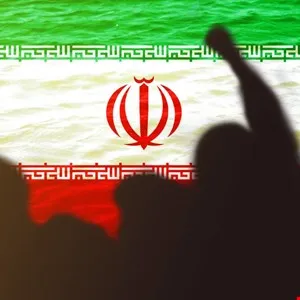 Silhouetted crowd with raised fist against Iranian flag backdrop.