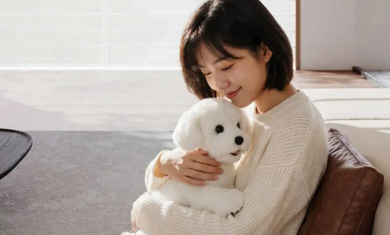 Woman gently holds a fluffy white robotic dog, smiling softly.