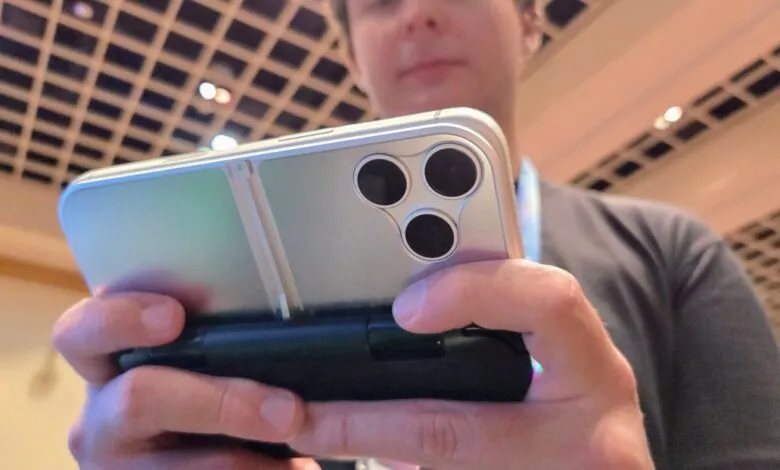 Person holds silver phone with triple camera and black controller attachment.