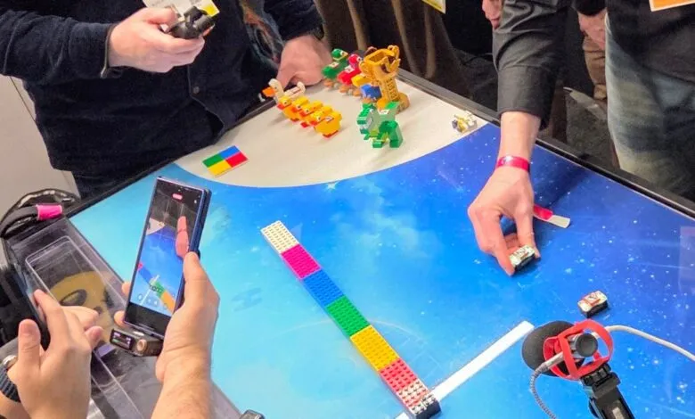 People interact with LEGO bricks on a digital table, filming with a phone.