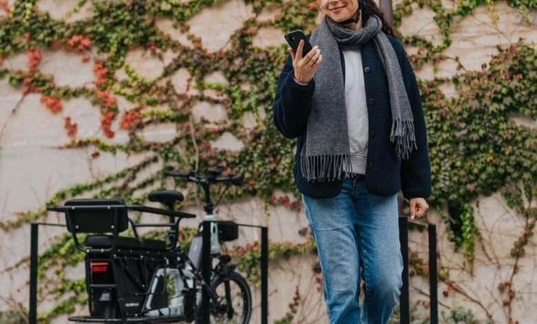 Woman checks phone next to electric bike against ivy-covered wall.