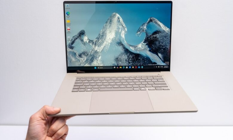 Asus Zenbook laptop held in hand, screen displays icy mountain scene.
