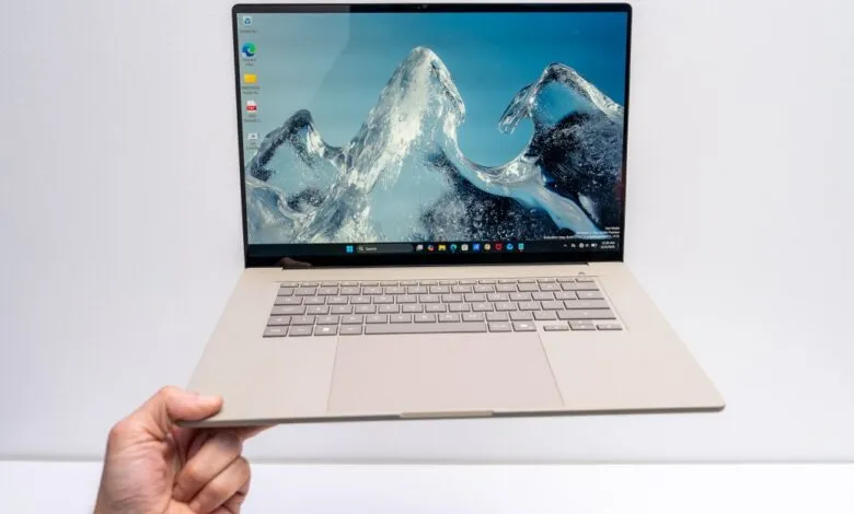 Asus Zenbook laptop held in hand, screen displays icy mountain scene.