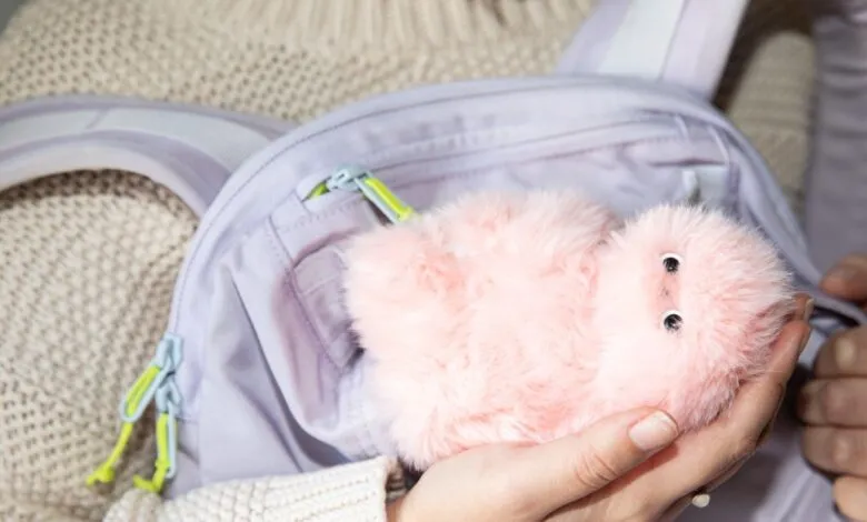 Person holding a pink, fuzzy toy in front of a lavender backpack.