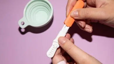 Hands preparing a hormone test kit with cup on purple background.
