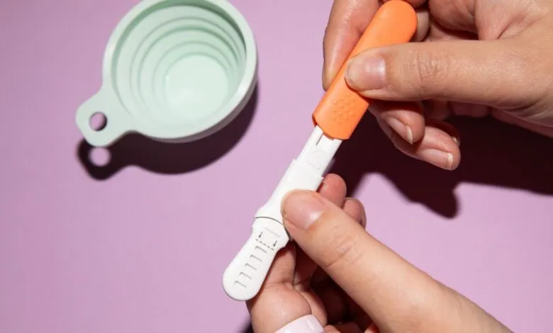 Hands preparing a hormone test kit with cup on purple background.