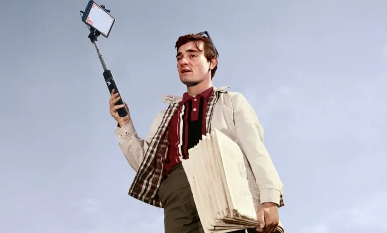 Nick Shirley holds papers and a selfie stick against a blue sky.