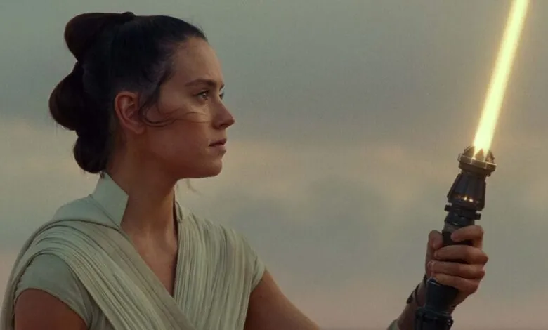 Daisy Ridley as Rey holding a yellow lightsaber, looking determined.