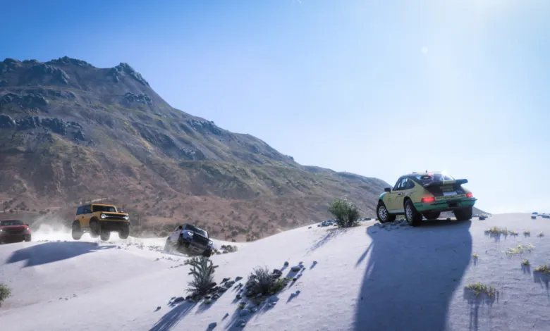 Off-road vehicles race across a sandy landscape with a mountain backdrop.