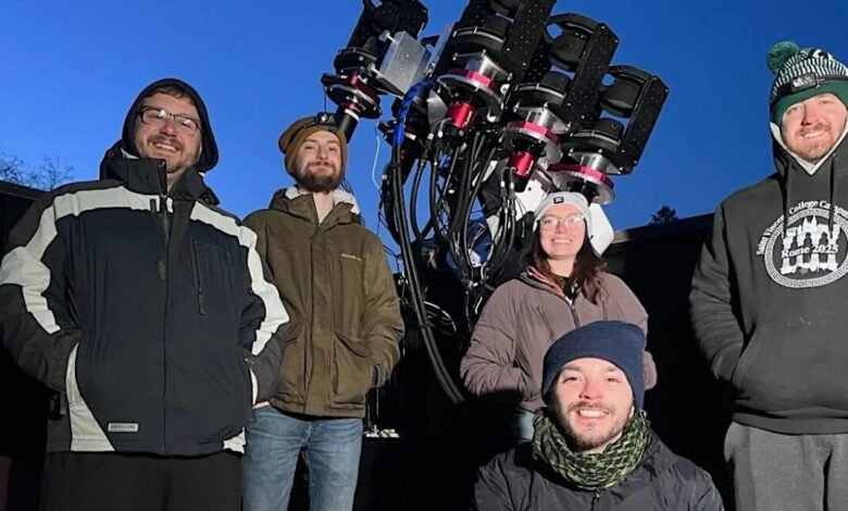 Group of five people posing with a large telescope under a twilight sky.