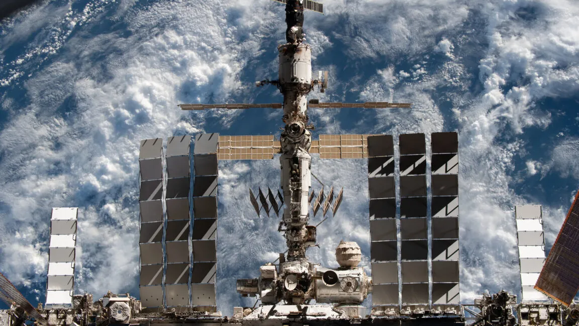 View of the International Space Station against a backdrop of Earth's clouds.