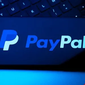 Close-up of the PayPal logo on a dark background, partially obscured by a keyboard.