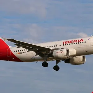 Iberia airplane in flight against a blue sky with scattered clouds.