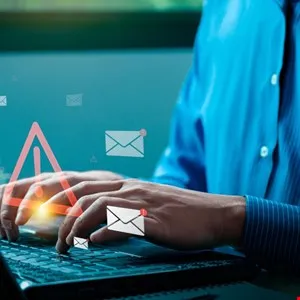 Person typing on laptop with email and warning symbols overlayed on the screen.