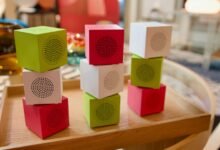 Colorful cube speakers stacked on a wooden tray, green, red, and white.