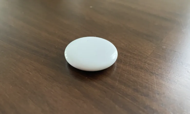 White Apple AirTag on a dark brown wooden surface.