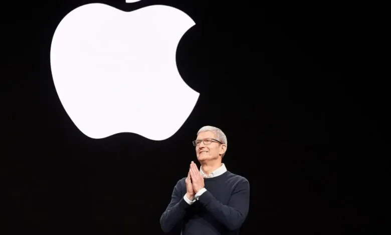 Tim Cook stands before a large Apple logo on a black background.