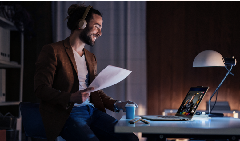 Man with headphones smiles during a video call at his desk.