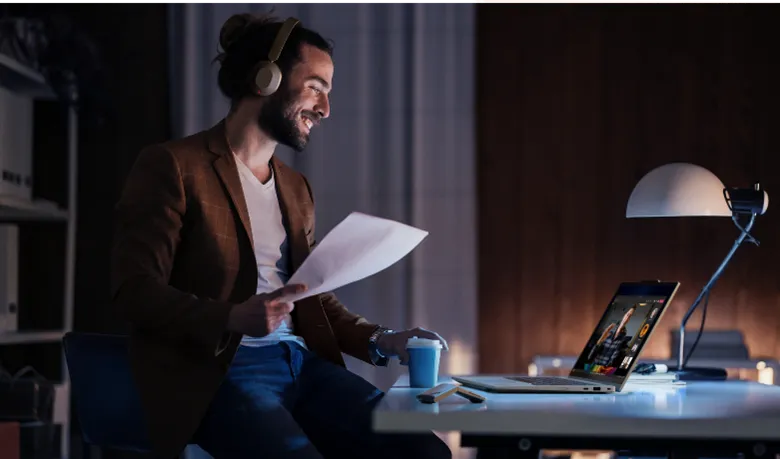 Man with headphones smiles during a video call at his desk.