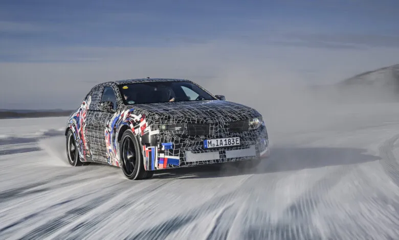 Camouflaged BMW electric car driving on ice, creating spray.