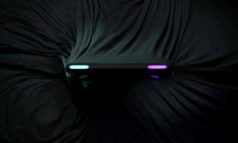 Sleek black device partially covered by dark fabric, neon lights visible.