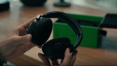 Hands holding black Razer gaming headphones with green box in background.