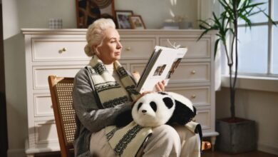 Woman reading magazine in chair with panda plush on lap.