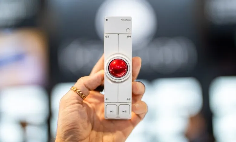 Hand holds white Keychron Nape Pro trackball with red ball.