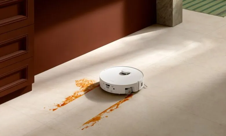 White robot vacuum cleaning up spilled sauce on a tiled floor.