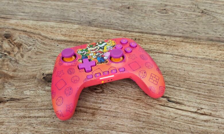 Pink Nintendo Switch controller with Mario characters on a wood surface.