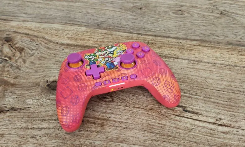 Pink Nintendo Switch controller with Mario characters on a wood surface.