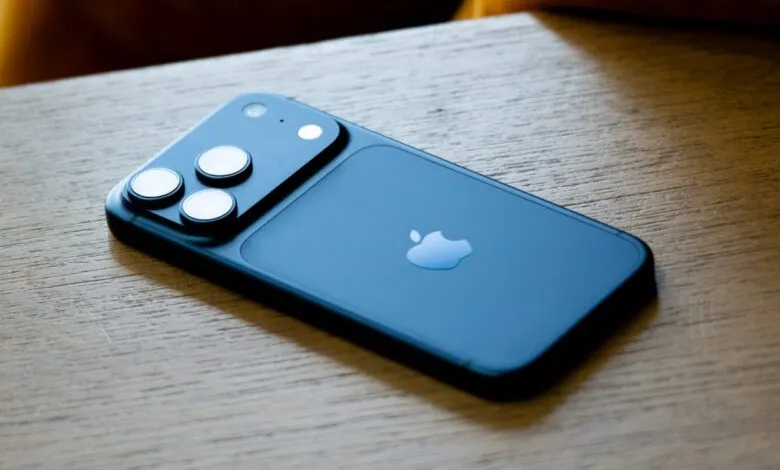 Back of a blue iPhone with three camera lenses on a wooden surface.