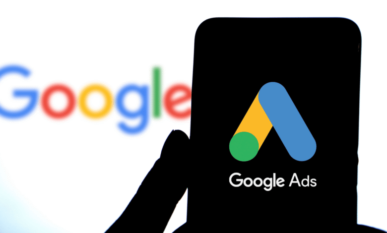 Google Ads logo on phone screen, Google logo blurred background.