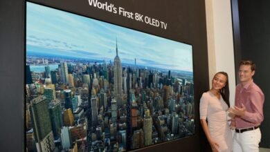 Couple admires 'World's First 8K OLED TV' displaying NYC skyline.