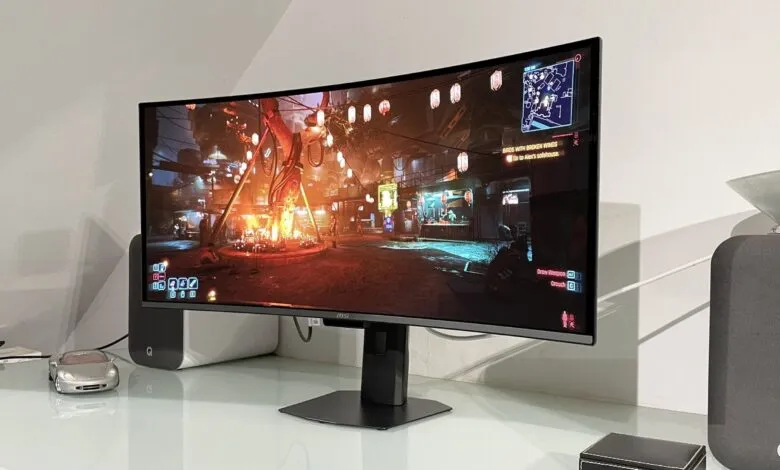 Curved MSI monitor displaying Cyberpunk 2077 gameplay, with speakers and car model.